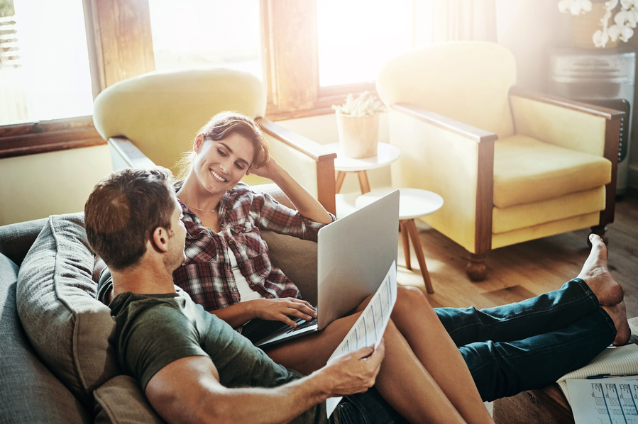 Happy couple, laptop and love on sofa for budget, planning and savings account for personal debt. Man, woman and together on couch with computer for expenses, tax and loan payment in living room.